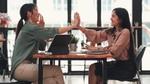 Two workers sitting at a table giving each other a high five