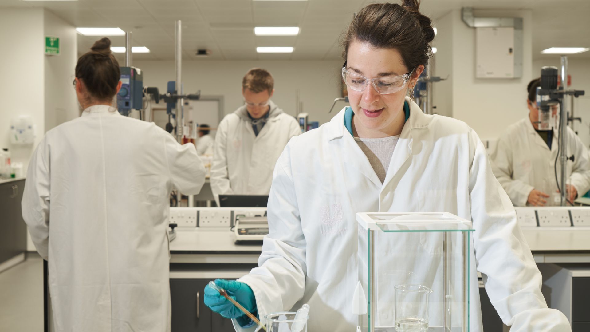A woman scientist at Unilever’s Port Sunlight fragrance R&D hub testing perfumes in the lab. She wears goggles and a white coat.