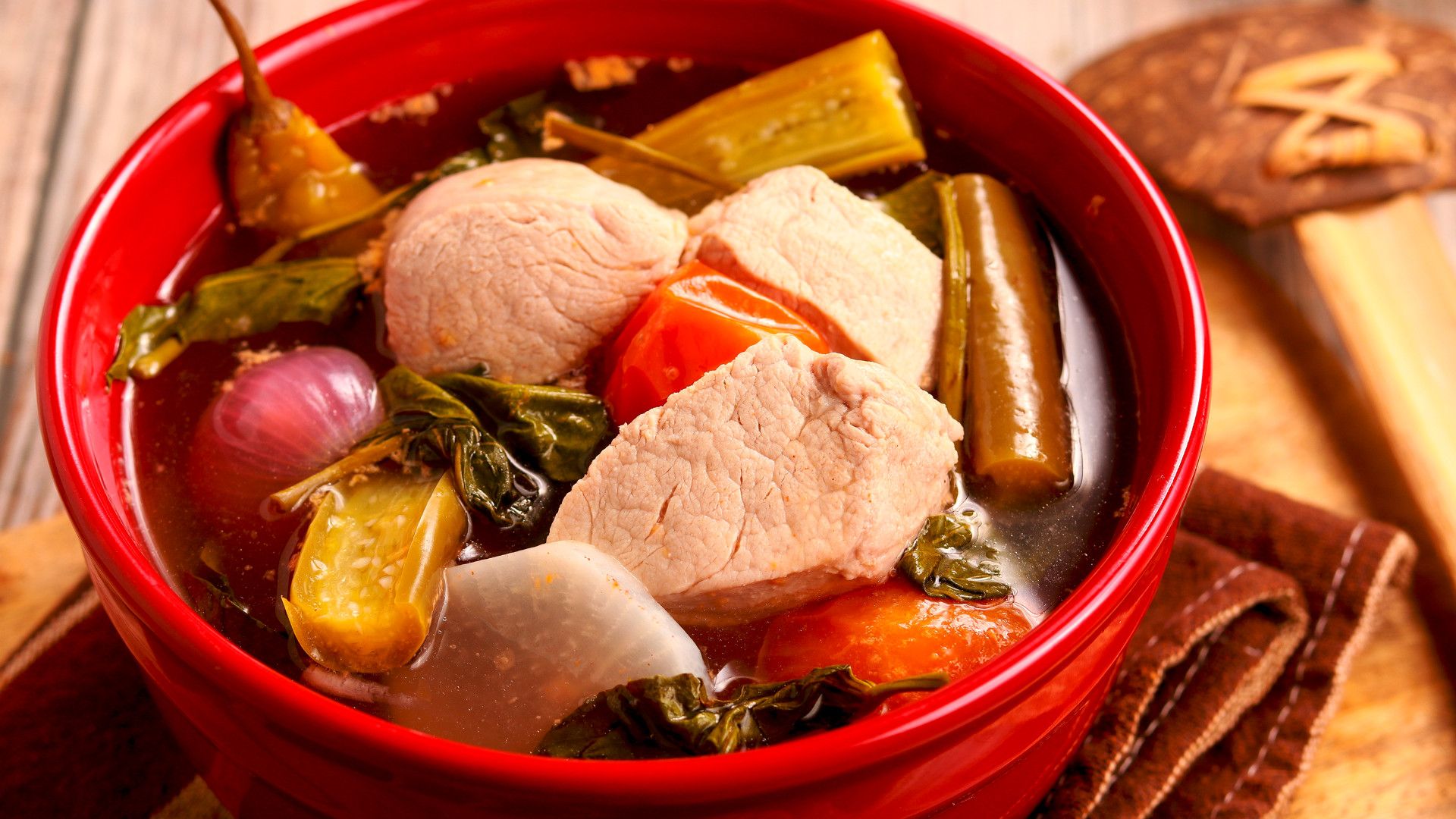 A bowl of hearty soup with chunks of meat, vegetables, and herbs.
