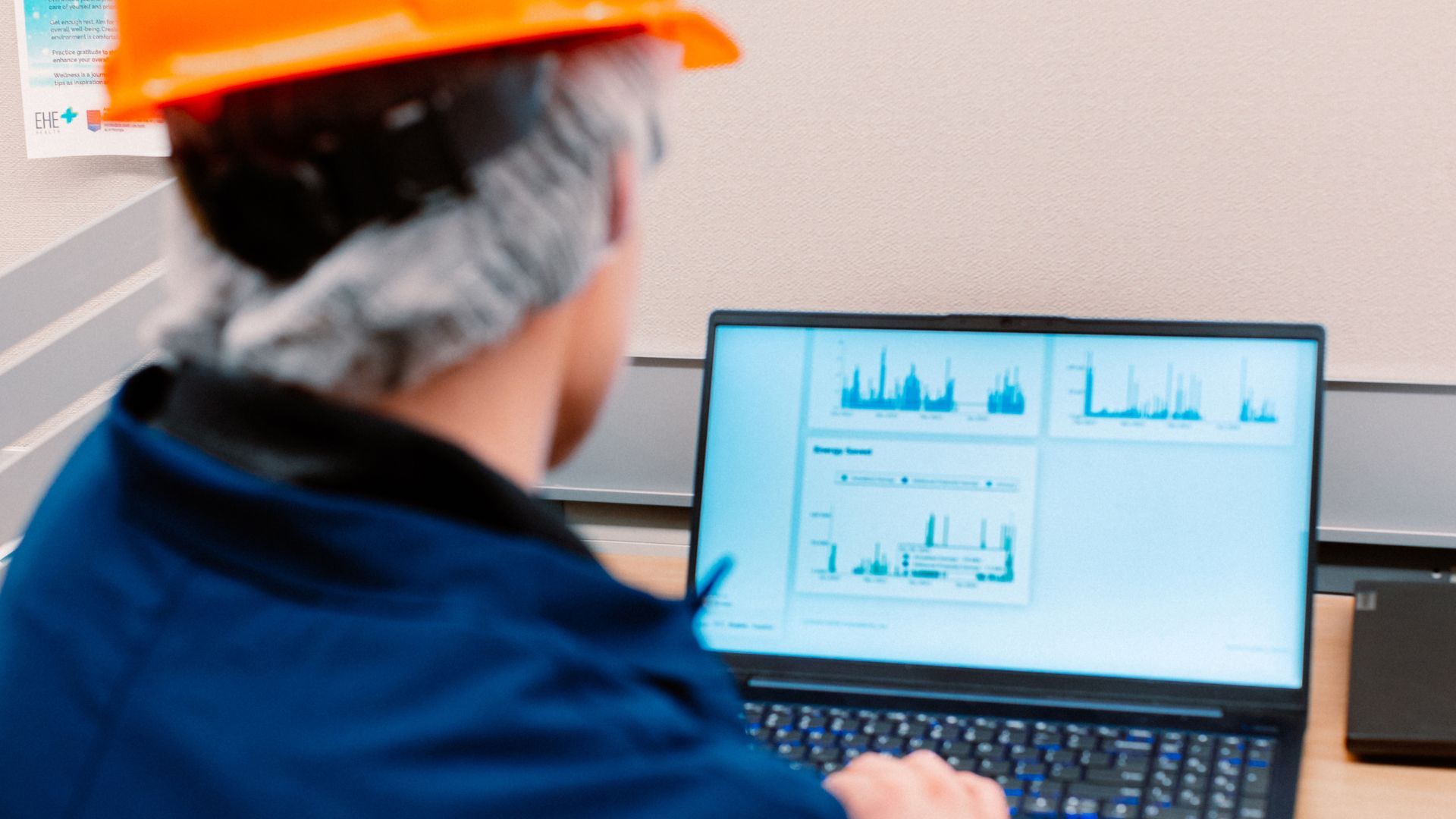 Factory worker in hard hat and navy-blue overalls facing a computer screen displaying data and H2Ok Innovation’s company logo