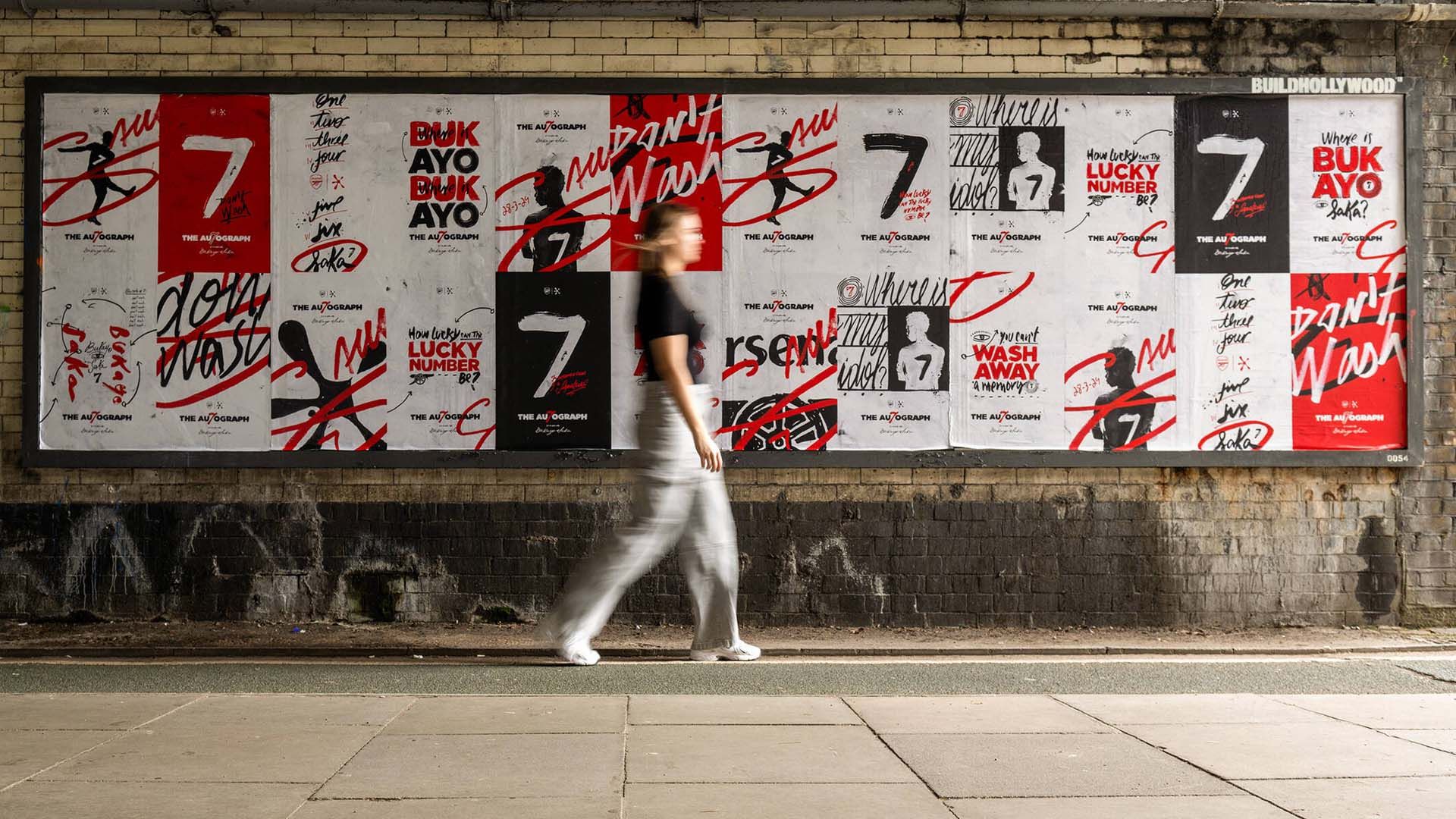 A woman walking past a brick wall covered in Persil Saka posters.