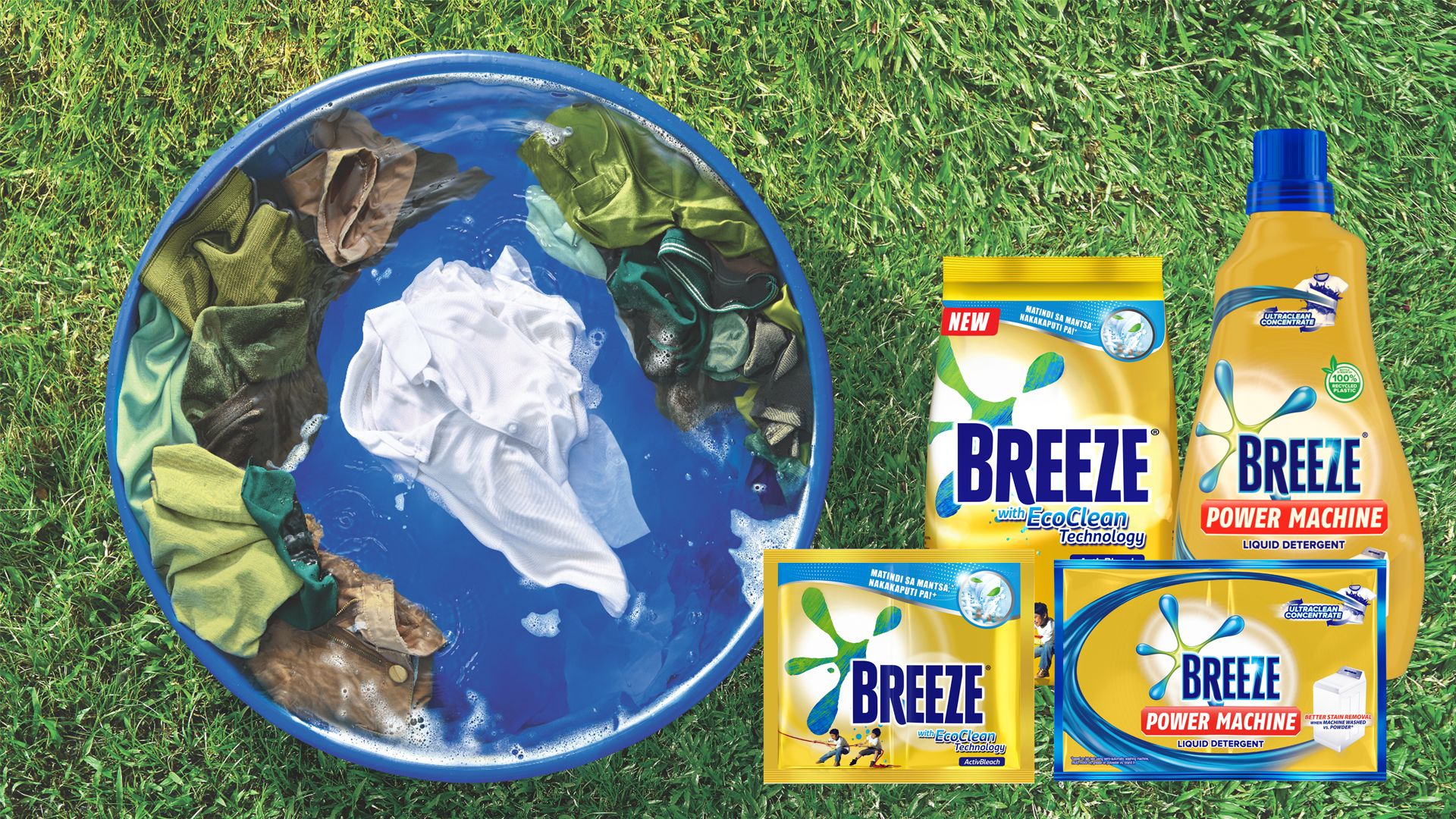 A laundry tub with green, brown and white clothes is placed on top of outdoor grass. Next to it are four Breeze products.