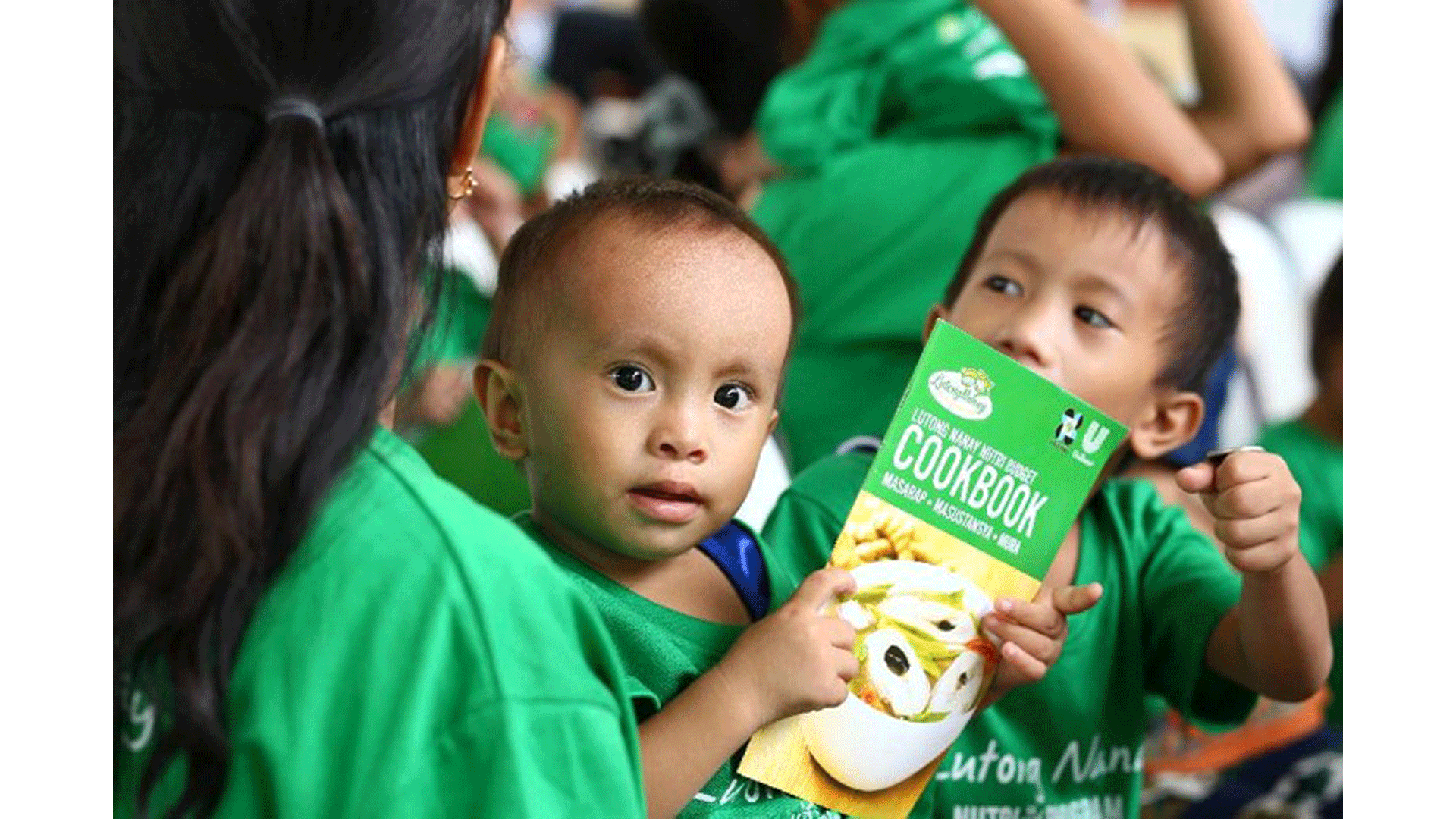 A child holds a Knorr Cook Book and seats on mother's lap