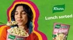 A woman with dark hair closes her eyes as she lifts a fork loaded with Knorr Mini meal Carbonara Pasta.