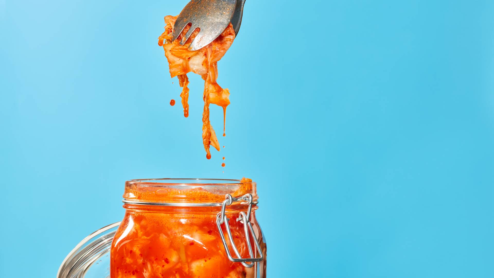 A stream of water splashes into a clear glass jar filled with green herbs and red and white striped beetroot slices.